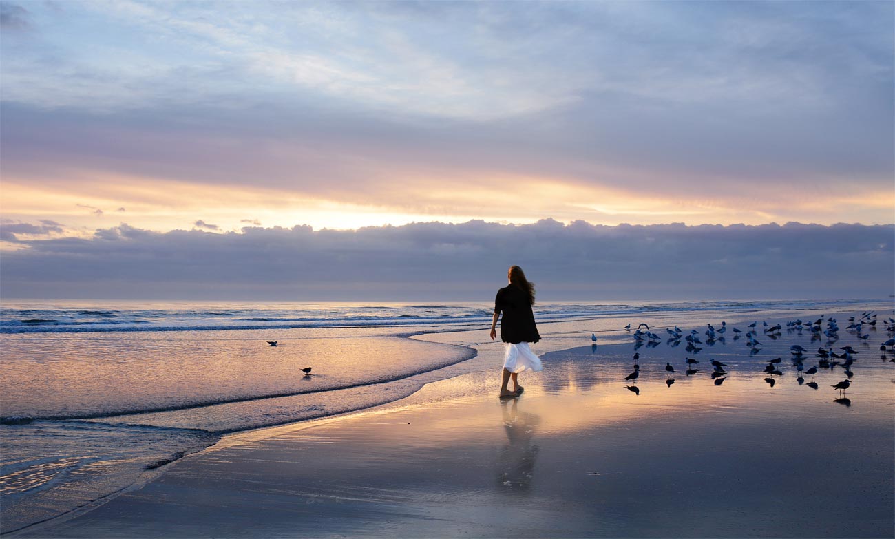 Girl-walking-on-the-beautiful-beach-at-sunrise-sun-and-clouds-reflected-in-the-water-on-the-beach-Daytona-Florida-USA.