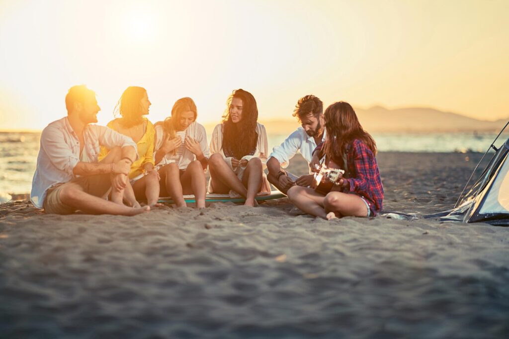 Group of young adults playing acoustic guitar at the beach
