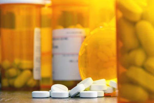 Prescription painkillers, oxycodone, spilling from a bottle on a table with other bottles out of focus