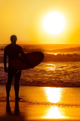 silhouette of a man carrying a surf board facing the ocean during sunset