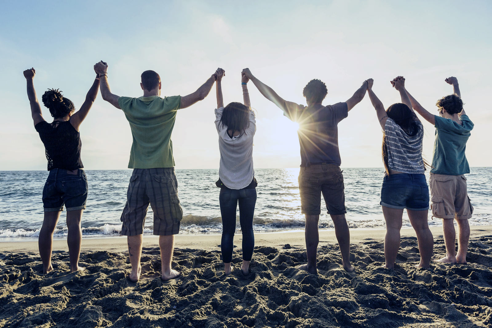 support group holding each other's hands up facing the ocean