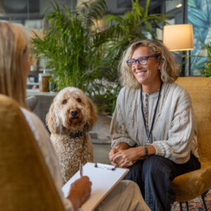 A woman with her labradoodle dog talking to her therapist at a dog-friendly rehab in California