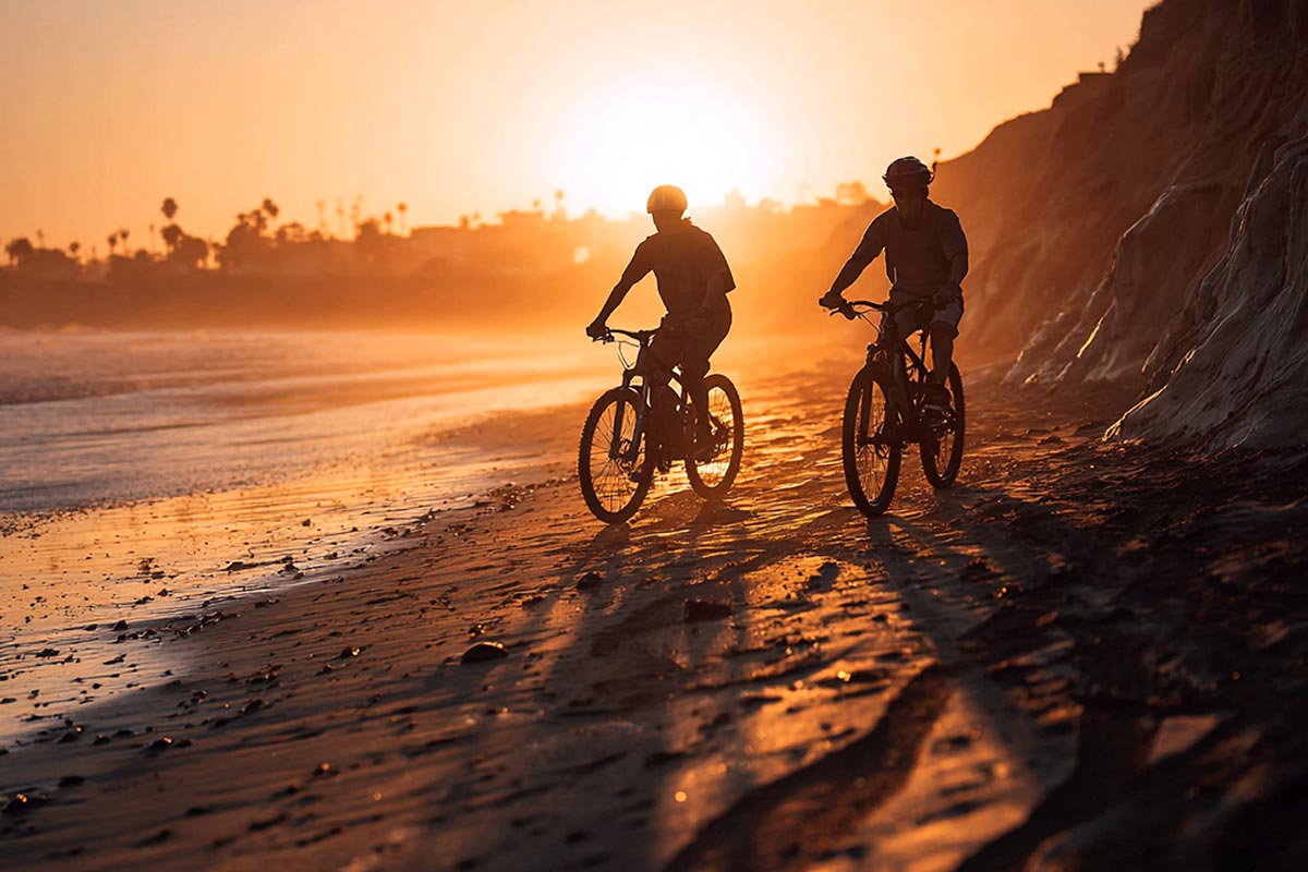 Two people riding bikes on the beach at sunset